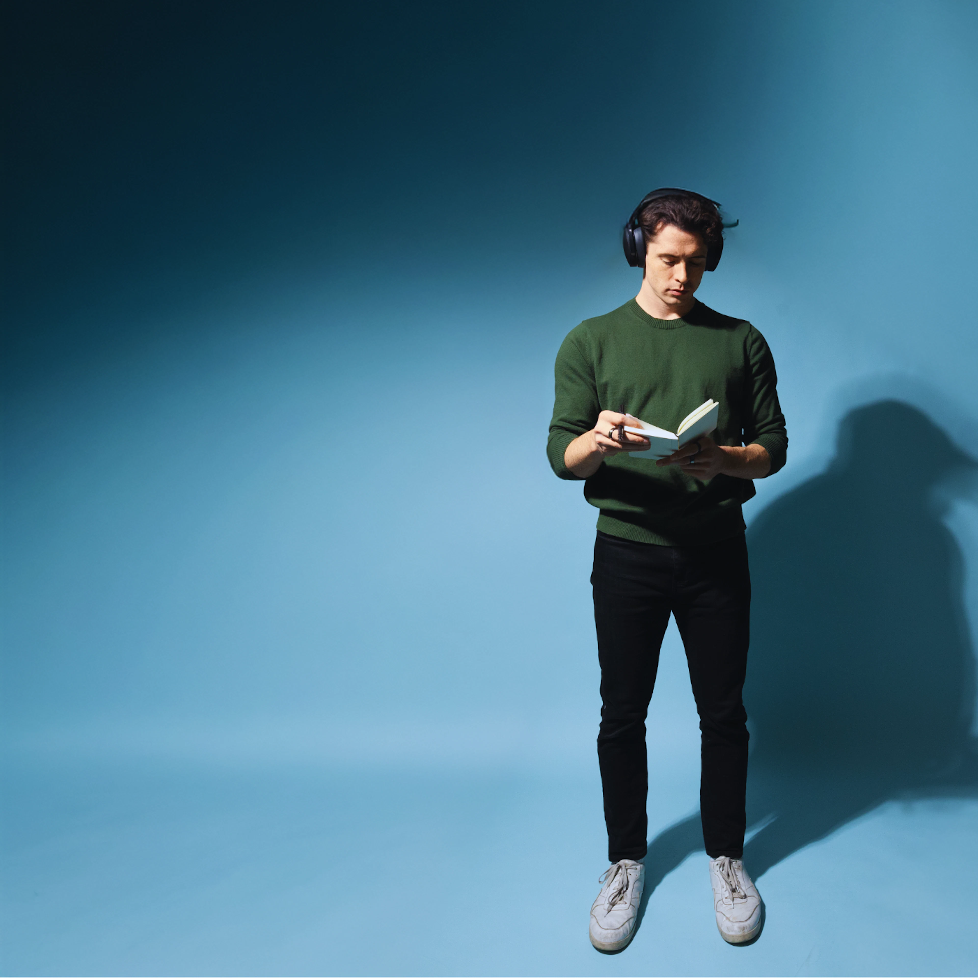 Maxwell Knowles reading with headphones against a blue backdrop